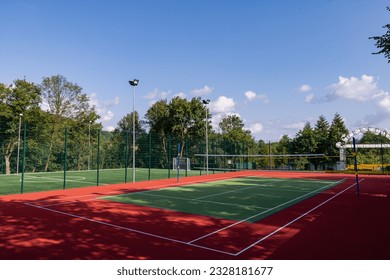 A sports field in a park with artificial grass and a stretched net against the background of green trees, with the morning rays of the sun, at dawn - Powered by Shutterstock