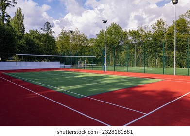 A sports field in a park with artificial grass and a stretched net against the background of green trees, with the morning rays of the sun, at dawn - Powered by Shutterstock