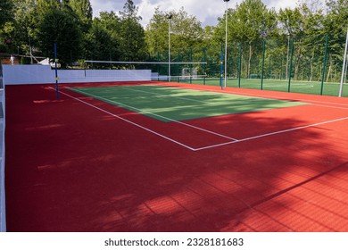 A sports field in a park with artificial grass and a stretched net against the background of green trees, with the morning rays of the sun, at dawn - Powered by Shutterstock