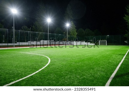 Sports field in the park with artificial grass stadium on the background of green trees. evening lighting with powerful lanterns, view from below