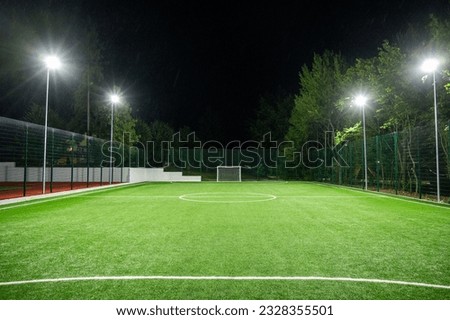 Sports field in the park with artificial grass stadium on the background of green trees. evening lighting with powerful lanterns, view from below