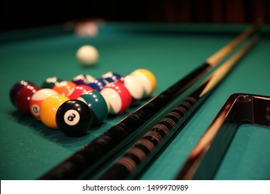 Sports game of billiards on a green cloth. Multi-colored billiard balls in the form of a triangle with numbers, two cues, a cue ball and a triangle on a pool table. Billiards billiard balls close up.