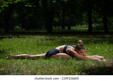 Sports girl acrobat performs acrobatic element on the grass in the Park