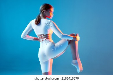 Sports girl raised leg holding knee by hand, rear view. Stretching workout, pilates, yoga studio. Long exposure - Powered by Shutterstock