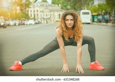 Sports girl with tattoo doing exercises on asphalt road, urban style