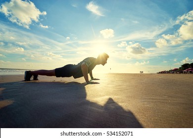 Sports and healthy lifestyle. Young man doing push-ups on the ocean beach. - Powered by Shutterstock