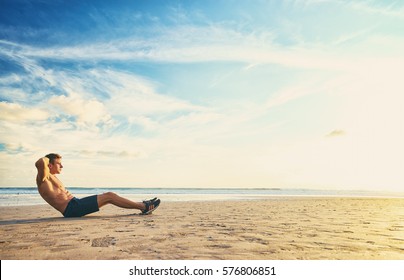 Sports And Healthy Lifestyle. Young Man Doing Crunches On The Ocean Beach.