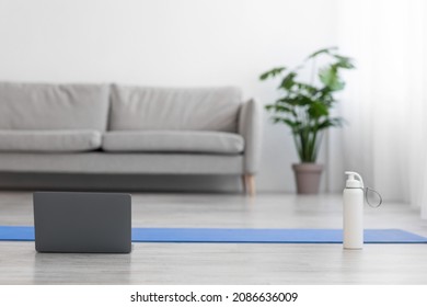 Sports At Home, Workout With Coach Remote In Modern Living Room Interior During Covid-19 Lockdown, Nobody. Laptop, Water Bottle, Mat On Floor, Sofa And Potted Plant On Gray Wall Background, Free Space