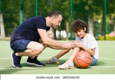 Sports Injury. Handsome PE teacher helping boy with knee trauma after playing basketball - Powered by Shutterstock