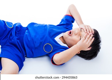 Sports Injury. Youth Asian (thai) Soccer Player In Blue Uniform Painful. Child Closed Eyes And Touching His Forehead. On White Background. Studio Shot. Boy Lie Down. Top View