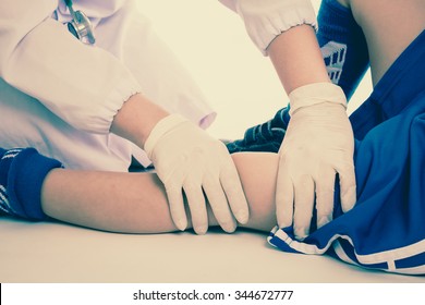 Sports Injury. Youth Soccer Player In Blue Uniform With Pain In Knee. Doctor Perform Checking And First Aid At Knee Trauma. Studio Shot. Cream Tones.