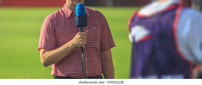 A Sports Journalist Broadcasts Live From A Football Field. Hand With A Microphone Closeup