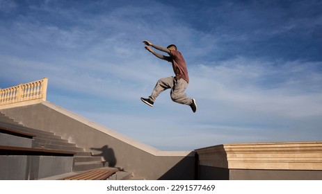 Sports man doing parkour against blue sky. Parkour athlete training in city in sportive clothes. Free runner jumping have workout at daytime. - Powered by Shutterstock