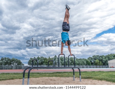 sports man handstand, balance, push-ups horizontal bar, exercise in city during summer, active lifestyle, modern fitness workout. Free space for motivation text. Background clouds and sports field