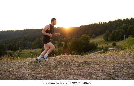 Sports man runner warming up before running or training on the top mountain at sunset. Good healtcare.