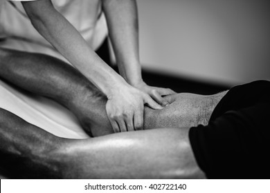 Sports Massage - Leg Massage - Physical Therapist Doing Massage Of Legs, Applying Strong Finger Pressure. Black And White Photo, Selective Focus.