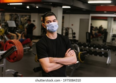 Sports Person In Protective Face Mask. A Personal Trainer Stands On The Background Of The Gym Wearing A Protective Mask