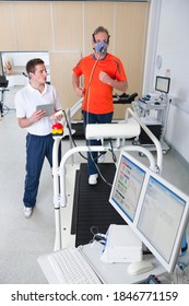 Sports Scientist With A Digital Tablet Monitoring A Senior Runner With Mask On A Treadmill In A Laboratory