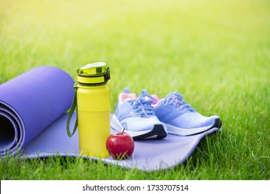 Sports shoes sneakers on yoga mat and water bottle, apple on fresh green grass. - Powered by Shutterstock