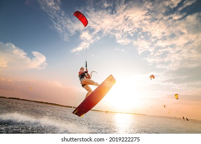 Sports shot of a young caucasian woman in a wetsuit doing a trick in the air against the backdrop of a sunset in the sea. Kitesurring girl athlete flies on a kite with a board