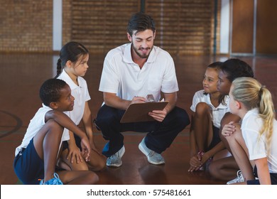 Sports teacher having discussion with his students in basketball court at school gym - Powered by Shutterstock