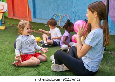 Sports teacher plays ball with children in physical education class outside in front of the day care center or after-school care center