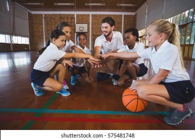 Sports teacher and school kids forming hand stack in basketball court at school gym - Powered by Shutterstock