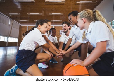 Sports teacher and school kids forming hand stack in basketball court at school gym - Powered by Shutterstock