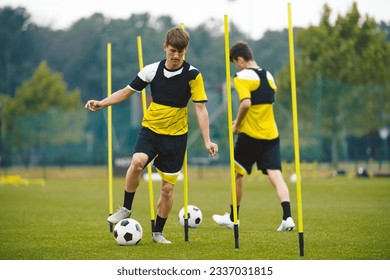 Sports Team on Training Camp Before the League Season. Group of Football Players Running With Balls in Between Training Poles on Training Pitch. Soccer Practice Session for Youth Footballers - Powered by Shutterstock