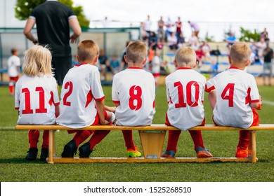 Sports Team On The Wooden Bench During The Youth Tournament On A Sunny Summer Day. Parents As Spectators Supporting Kids In The Background