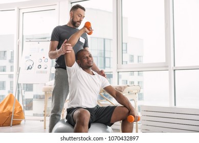 Sports Therapy. Pleasant Good Looking Man Exercising With Dumbbells While Being In The Gym