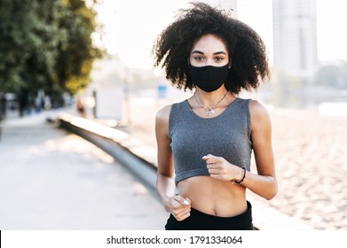 Sports training outdoor in safety during epidemic, quarantine. An African-American woman jogs with a medical mask on the face. Close-up portrait, copy space - Powered by Shutterstock