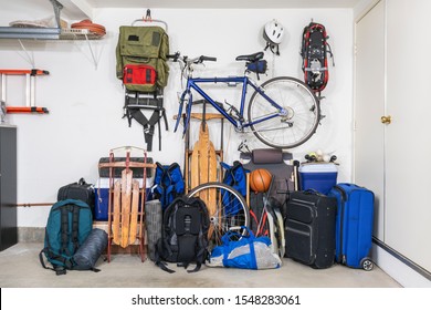 Sports And Travel Gear And Equipment In Piles In Corner Of Messy Suburban Garage.