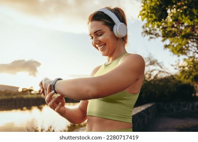 Sports woman choosing a fitness playlist using a smartwatch outdoors. Happy woman going for a morning run with headphones. Woman using technology for a workout. - Powered by Shutterstock