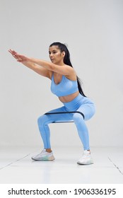 Sports woman in fashion clothes squatting with fitness resistance band. Healthy lifestyle concept.