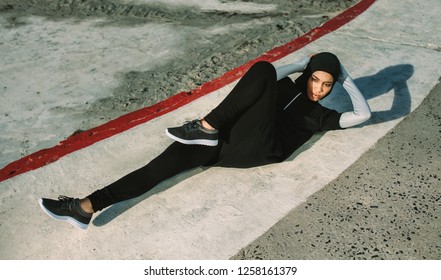 Sports woman in hijab doing bicycle crunch workout outdoors. Female lying on concrete floor and doing abs workout exercises in morning. - Powered by Shutterstock