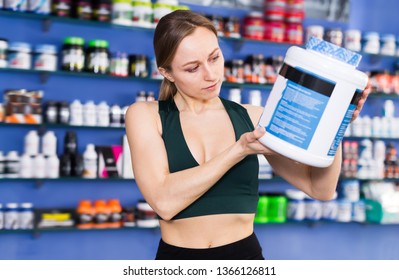 Sports Woman Holding Plastic Jar With Sport Nutrition, Reading Label Carefully Before Buying In Shop