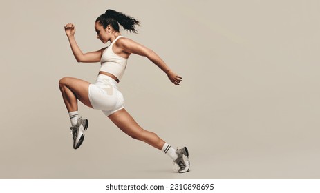 Sports woman jumping forward, running in a studio workout. Wearing sportswear, she combines strength training with cardio exercises to improve fitness. Female athlete pushing herself to new limits. - Powered by Shutterstock