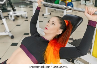Sports young woman doing exercises with barbell on bench in the gym. Bar Bench Press. Athlete female doing exercises with a bar lying down in the gym. Classes at the sports club