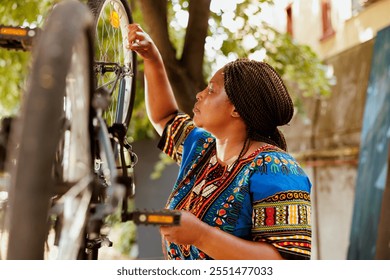 Sports-loving african american woman holding professional equipment for bike maintenance in home yard. Determined young female cyclist focuses on repairing bicycle wheel with specialized spanner. - Powered by Shutterstock