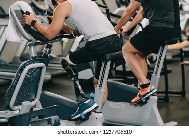 Sportsman With Artificial Leg Working Out On Stationary Bicycle At Gym