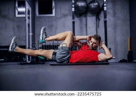 Sportsman doing bicycle lateral crunch workout at the gym. A hot male person in a fitness club doing sit-up exercises. Fitness goal, sport lover, legs extension