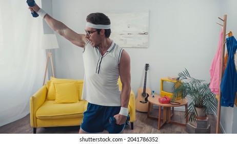 Sportsman In Eyeglasses And Retro Sportswear Lifting Dumbbells At Home