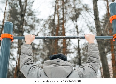 Sportsman Hanging On Horizontal Bar Outside In Winter. Man Pulls Up On Sports Equipment. Winter Training. Back View