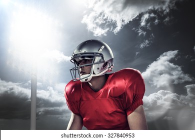 Sportsman holding American football while kneeling against spotlight in sky - Powered by Shutterstock