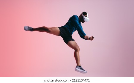 Sportsman jumping mid air while wearing a virtual reality headset. Athletic young man experiencing a 3D simulation. Man enjoying a virtual training session against a studio background. - Powered by Shutterstock