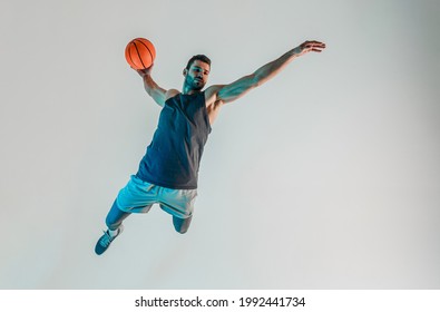 Sportsman jumping and want throw basketball ball. Serious young bearded european basketball player. Isolated on turquoise background. Studio shoot. Copy space - Powered by Shutterstock