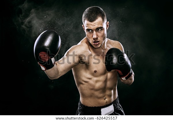 Sportsman muay\
thai boxer fighting in gloves in boxing cage. Isolated on black\
background with smoke. Copy\
Space.