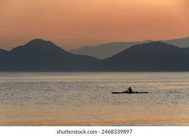 Sportsman paddling canoe in the sea during sunset. In the background the silhouette of the mountains. City of Santos, Brazil. - Powered by Shutterstock