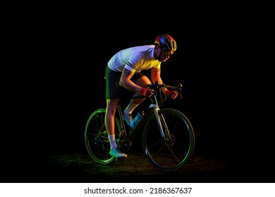 Sportsman. Portrait Of Young Male Cyclist On Bicycle In Cycling Shorts And Protective Helmet Isolated On Dark Background In Neon Light. Concept Of Active Life, Rest, Travel, Energy, Sport.